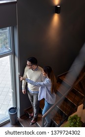 Couple In Love On A Date, Walking Down The Restaurant Stairs, Holding Hands, Looking Through The Window And Pointing At Something Outside