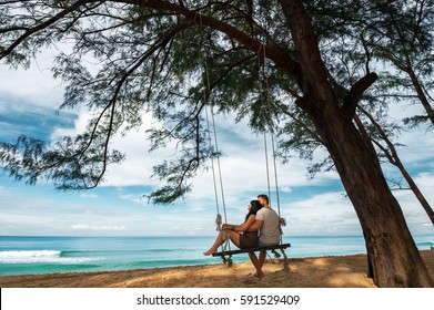 Couple in love on a swing by the sea. Couple in love on an island off the coast. Honeymoon. Couple by the sea. Man and woman travel to beautiful places. Honeymoon trip. Relax on the island. In love