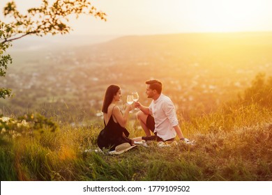 Couple in love on a white plaid take a picnic against the backdrop of a sunset in the mountains. Romantic time. Beautiful couple is enjoying picnic time at sunset.  Copy space. - Shutterstock ID 1779109502