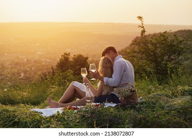 Couple In Love On A White Plaid Take A Picnic Against The Backdrop Of A Sunset In The Mountains. Romantic Time. Beautiful Couple Is Enjoying Picnic Time At Sunset. Copy Space.