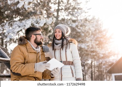 Couple in love on a winter vacation taking photos with a tablet computer outdoors on a sunny, snowy day. Focus on the girl