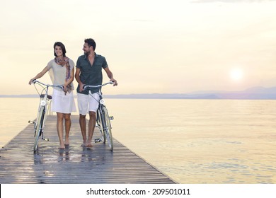 couple in love pushing bike on a boardwalk at the lake at sunset