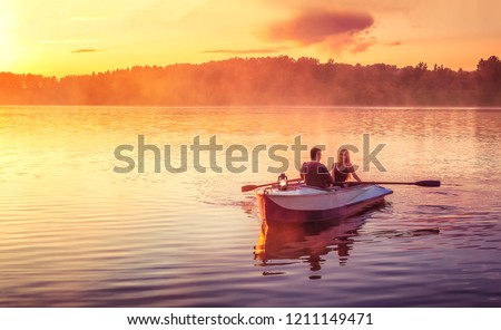 Couple in love ride in a rowing boat on the lake during sunset. Romantic sunset in golden hour. Happy woman and man together relaxing on water nature around