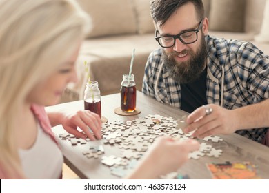 Couple in love sitting on the floor next to a table, solving a jigsaw puzzle problem and enjoying their leisure time activities. 
