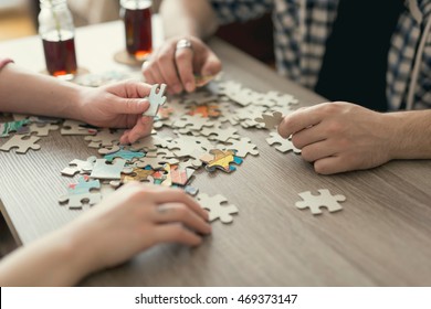 Couple in love sitting on the floor next to a table, solving a jigsaw puzzle problem and enjoying their leisure time activities. 