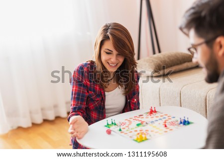 Couple in love sitting on the floor next to a table, playing ludo board game and enjoying their free time together. Woman rolling the dice