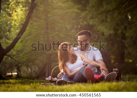 Couple in love sitting on a picnic blanket in a park, talking to each other, drinking wine and enjoying a beautiful, peaceful day in nature