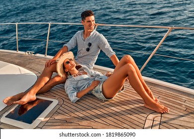 Couple in love sitting on yacht deck while sailing in the sea. Handsome man and beautiful woman having romantic date. Luxury travel concept.