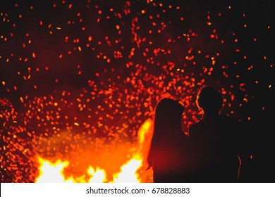 Couple in love standing in front of big fire and looking at sky 