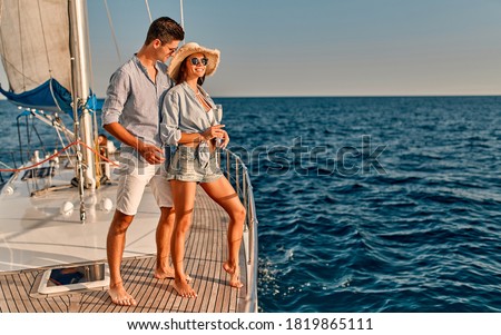 Couple in love standing on yacht deck while sailing in the sea. Handsome man and beautiful woman having romantic date. Luxury travel concept.