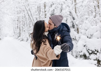 Couple Love Story In Snow Forest Kissing And Holding Sparklers. Couple In Winter Nature. Couple Celebrating