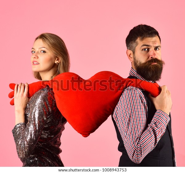 Couple in love tears big heart on pink\
background. Girl and bearded man with serious faces divide soft toy\
heart with hands. Boyfriend and girlfriend have break. Love symbol\
and dating concept.