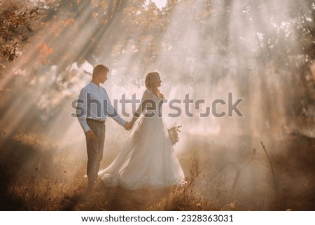 Couple in love together holiday wedding day marriage concept. Happy man woman walking in forest autumn nature magical sun light rays flare fog mist. Lady bride in long light gray dress, groom suit