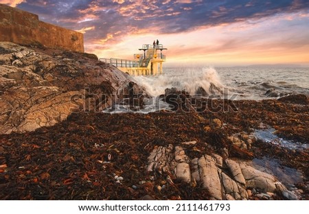 Couple in love under dramatic cloudy sunset sky at Blacrock diving tower on Salthill beach in Galway, Ireland 