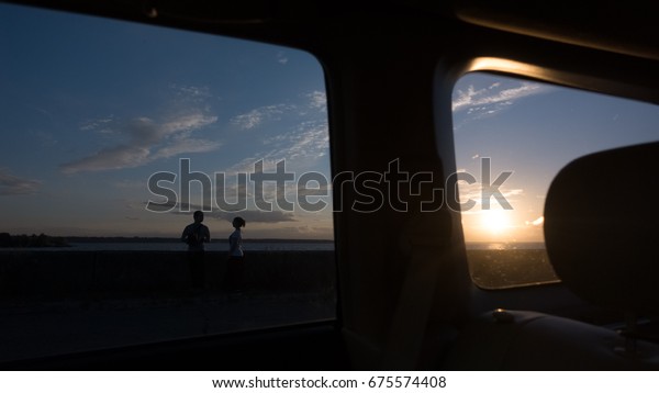 Couple in love watching the sunset at\
the sea through the side and rear window of the\
car