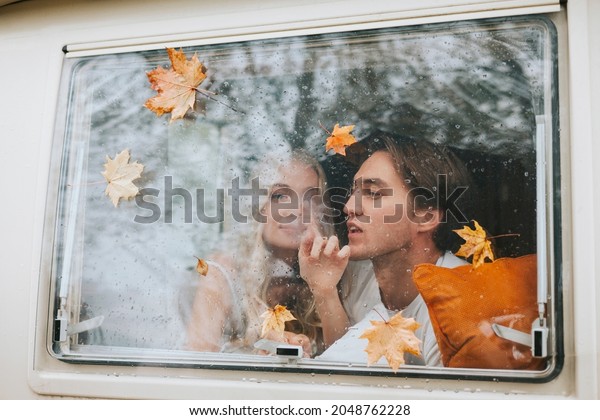 couple in love from window with rain drops and\
autumn leaves having fun together, young man and woman newlyweds\
hugging on bed in trailer mobile home or recreational vehicle\
during family local\
travel