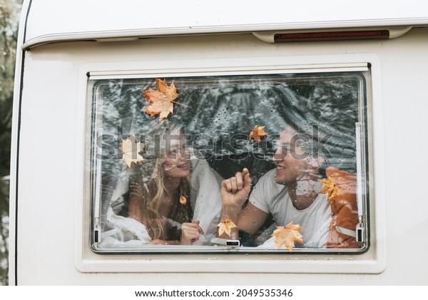 couple in love from window with rain drops and\
autumn leaves having fun together, young man and woman newlyweds\
hugging on bed in trailer mobile home or recreational vehicle\
during family local\
travel