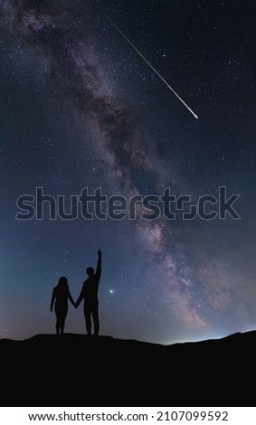 A couple of lovers hold hands and look at a shooting star at night against the backdrop of the Milky Way. No focus in the foreground, such an idea. Silhouettes are drawn by hand without reference.