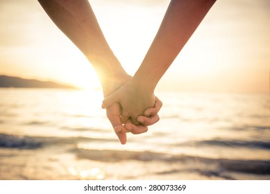 Couple of lovers holding their hands at a beautiful sunset over the ocean - Newlywed couple on a romantic vacation