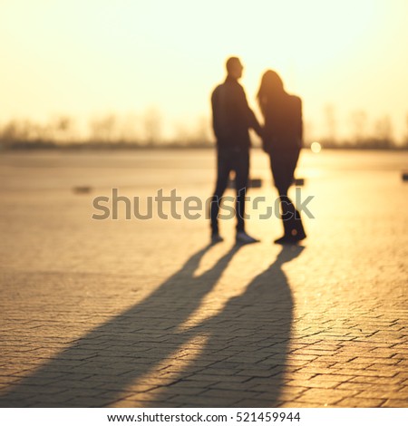 Couple of lovers on the cobblestone pavement at sunset. Long shadow