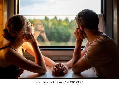 Couple of lovers traveling in train. Mood portrait of loving romatic pair in wagon looking at window with self reflections in it. Adventure on vacation of happy family. Man holding woman`s hands.