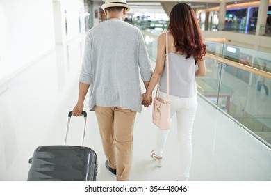 Couple With Luggage Walking In Airport, View From The Back