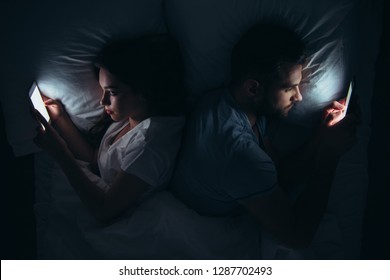 Couple Lying Back To Back In Bed And Using Smartphones At Night