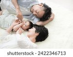 A couple lying down in the living room with their baby Overhead view