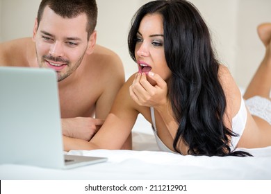 Couple lying with laptop in bed and watching porn movie