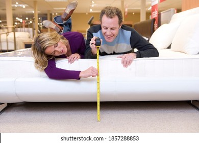 Couple lying on a bed and measuring the distance of the top from the ground with a measuring tape in the furniture shop