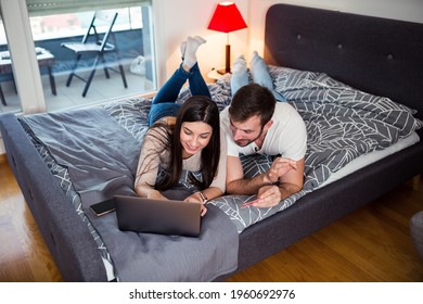 Couple lying on bed and using laptop