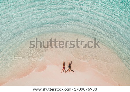 Couple lying on famous pink beach in Komodo national park. Turquoise mint color clear water, tropical vacations on honeymoon. Drone aerial view from above.