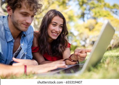 Couple lying on grass and using laptop in park on a sunny day - Powered by Shutterstock