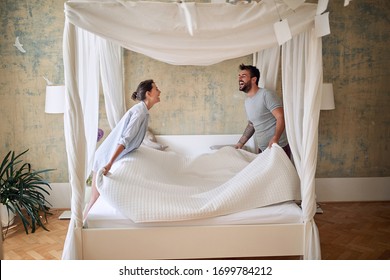 Couple making bed.Charming smiling man and woman in love making bed together.