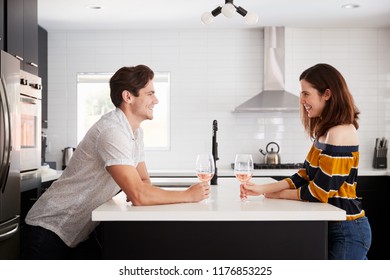 Couple Making Drinking Wine At Home Standing By Kitchen Island