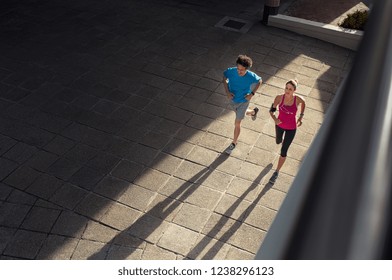 Couple Making Fitness And Jogging In The Urban Area Of The City. High Angle View Of Two Mature People Training Together On Road. Fitness Man And Woman Running On City Street.