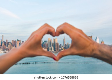 Couple making a heart shape with hands with New York skyline on background. Man and woman in love in New York. Travel and lifestyle concepts in the most famous city of United States of America