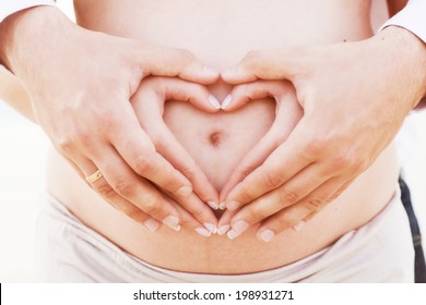 A couple making a heart shape on the pregnant belly with their hands. Concept of pregnancy, expecting a baby, love, care.