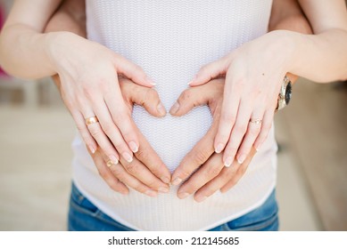 A couple making a heart shape on the pregnant belly with their hands. Concept of pregnancy, expecting a baby, love, care. - Powered by Shutterstock