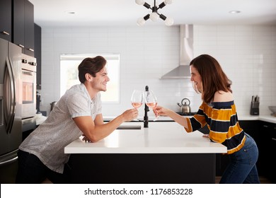 Couple Making Toast As They Drink Wine At Home Standing By Kitchen Island - Powered by Shutterstock