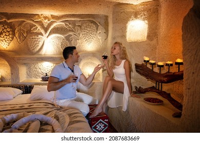 A Couple Man And Woman Drinking Red Wine In The Old Cave Room Of Cappadocia On The Carved Bed With Vines