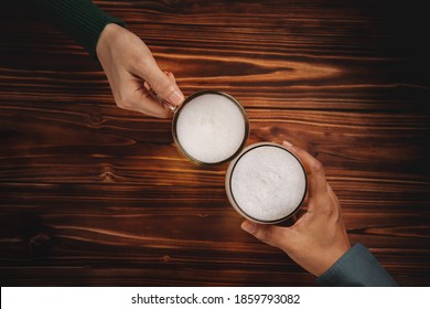 Couple of Man and Woman or Friends holding a Glass of Beer to Celebrate in Restaurant or Bar, For Oktoberfest or any Cheerful Event Concept, Top View on Wooden Table