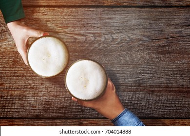 Couple of Man and Woman holding a Glass of Beer to Celebrate in Restaurant or Bar, For Oktoberfest or any Cheerful Event Concept, Top view Over Wooden Table