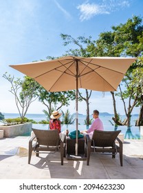 Couple Man And Woman Mid Age At A Luxury Beach Chair, On A Luxury Vacation In Thailand, Men And Asian Woman In Pool Looking Out Over The Bay Watching Sunset. Infinity Pool Over Ocean