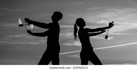 Couple of man and woman perform burning poi dance during fire performance in dark silhouettes on idyllic evening sky outdoors, fiery