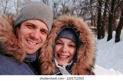 Couple Man And Woman Talking On Video Connection And Walking In Winter City Park In Snowy Day With Falling Snow.