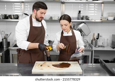 Couple, a man and a woman temper the chocolate and measure the temperature with a non-contact thermometer. - Shutterstock ID 2155778329