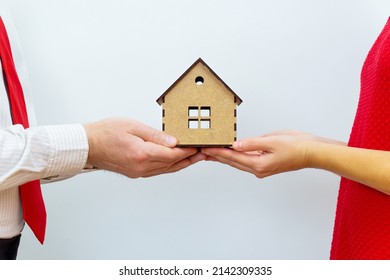 Couple In Matching Outfits Holding A Miniature House Model In Hands. Buying A Family Home Together.