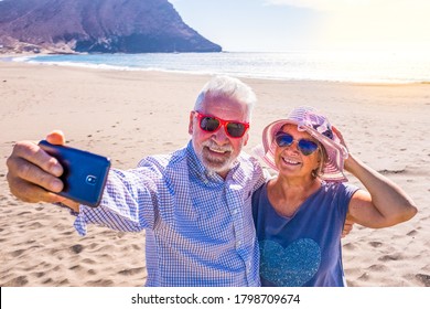 couple of mature people or pensioners enjoying their vacations and summer time together on the sand of the beach with the sea or ocean at the background - two retired senior taking a selfie smiling - Powered by Shutterstock