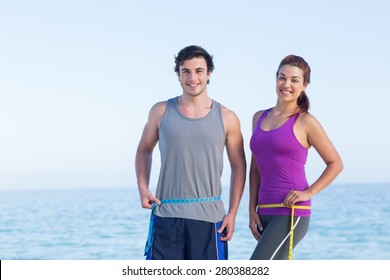 Couple measuring their waist at the beach
